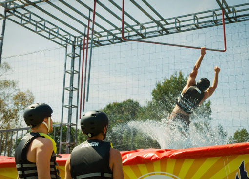 Deux personnes regardent un ami qui tombe dans une piscine du parcours Go Ninja